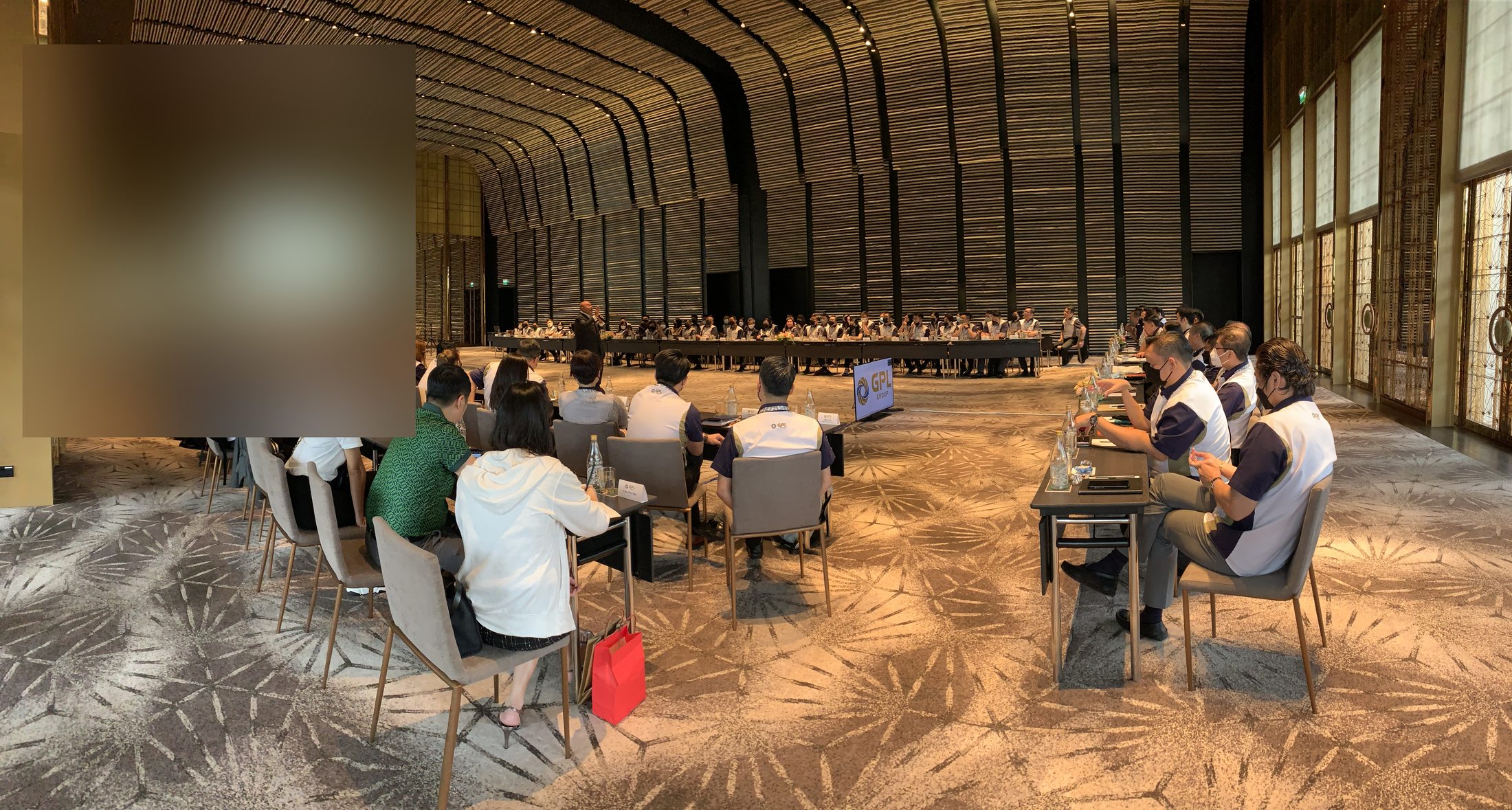 Ultra-wide panoramic — 80+ participants in a luxury ballroom, Marcus Lim presenting from the floor
